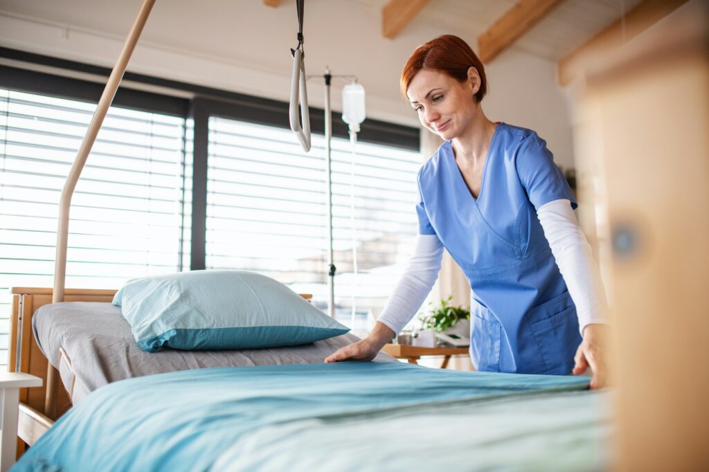 Portrait of female nurse or housekeeping staff changing sheets in hospital.